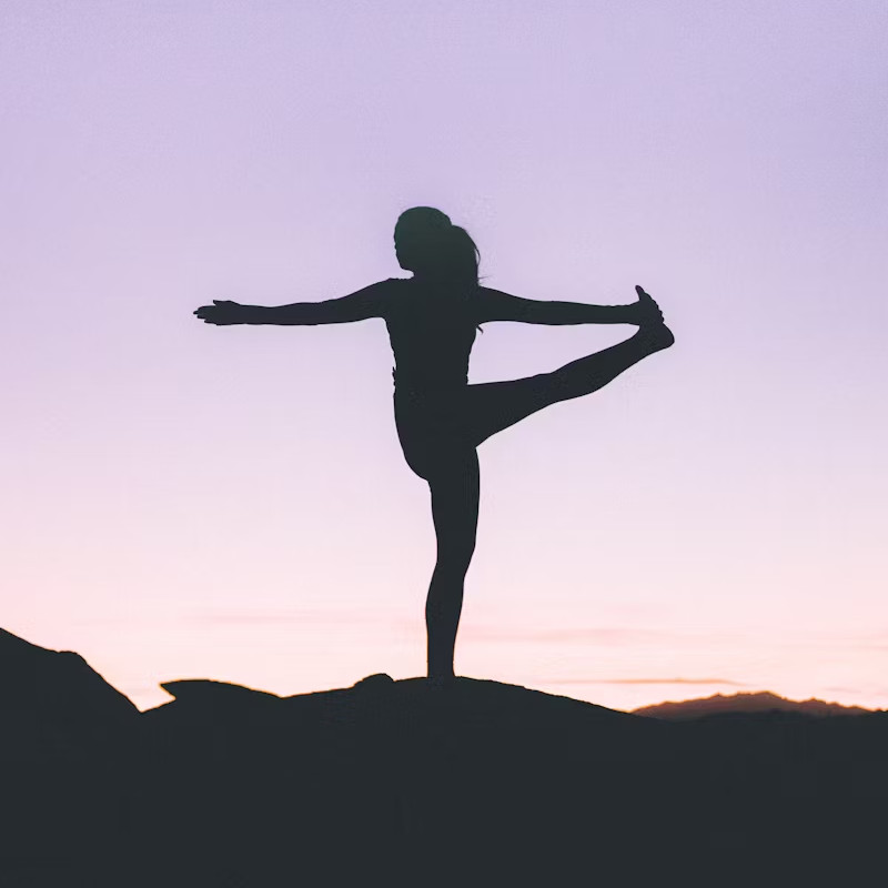 A woman practicing yoga on a mountain peak, surrounded by breathtaking views and clear blue skies.